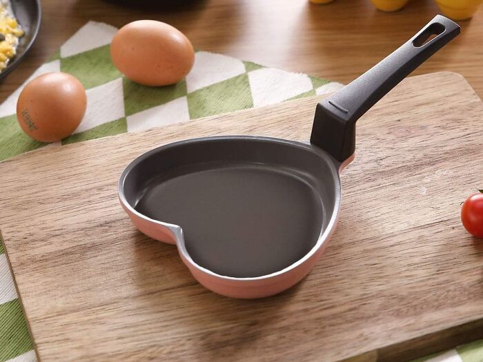 Heart-shaped frying pan on a wooden board with eggs; combines usefulness with aesthetic appeal.