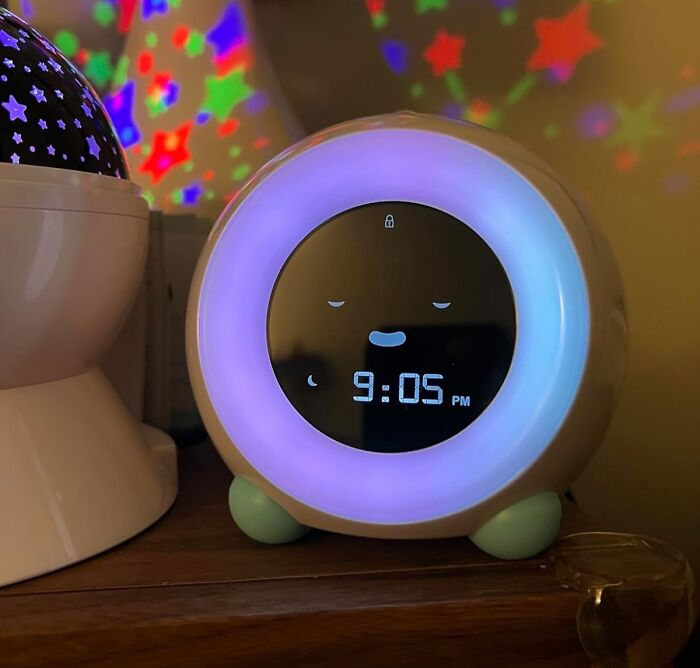 Smart digital clock with glowing purple light and star projections, a device that works hard and looks good on a wooden surface.