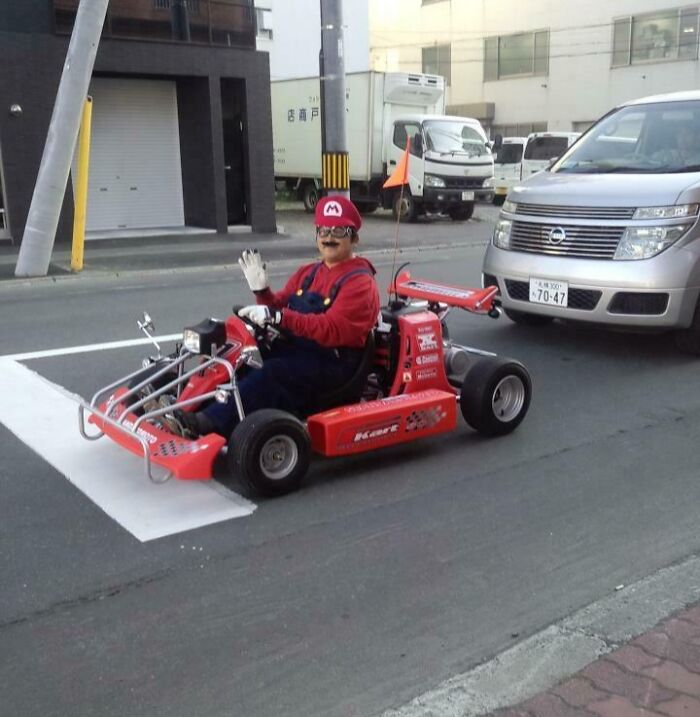 Person dressed as Mario driving a go-kart on a street in Japan, featuring an interesting scene.