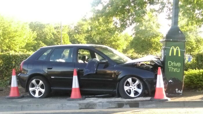 Car crashed into a McDonald's drive-thru sign, surrounded by cones, illustrating hilarious misunderstandings in navigation.