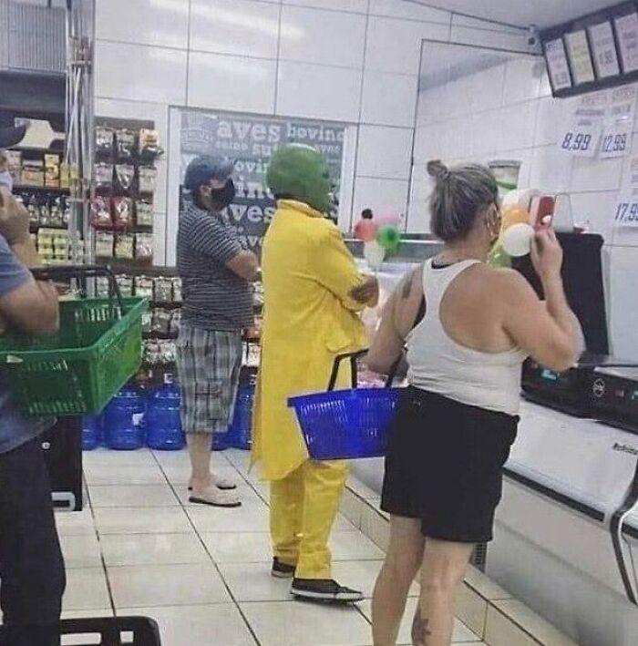 Person in a yellow suit and green mask shopping at a supermarket, surrounded by other shoppers. Hilarious misunderstandings.