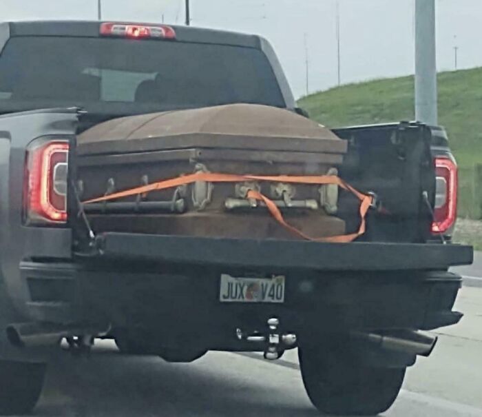 Pickup truck with a casket in the bed, secured by orange straps on a Florida road.