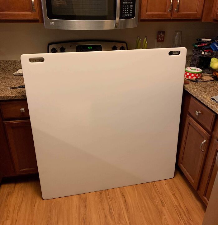 Large cutting board hilariously misunderstood as a dishwasher, leaning against kitchen counter.