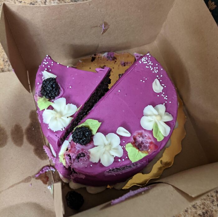 Wedding guest cake mishap with a missing slice, decorated in purple with flowers and berries.