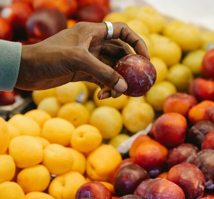 Hand selecting fresh fruits including plums and apricots.