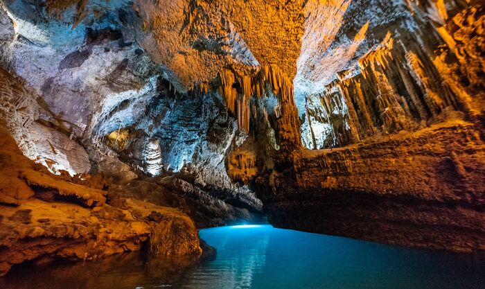 Stunning natural wonder cave with illuminated stalactites and blue water.