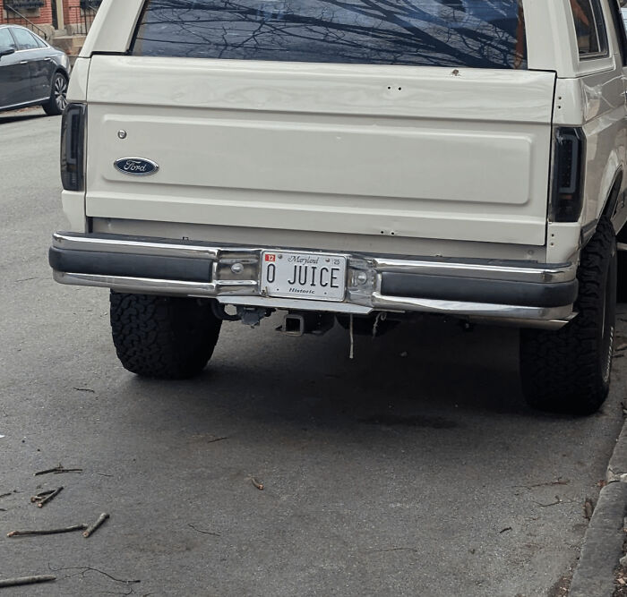 White '90s Ford SUV with a personalized "O JUICE" license plate parked on a street.
