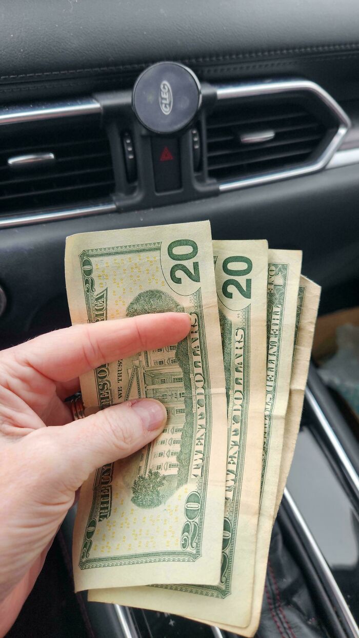 Hand holding several twenty-dollar bills, showcasing a lucky find while thrifting.