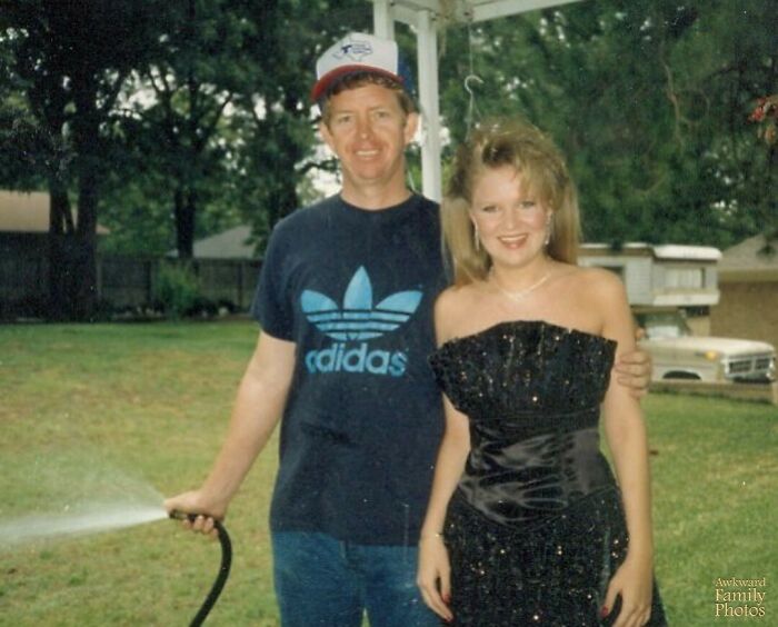 Man in casual clothes holding a garden hose next to a woman in a formal dress, an awkward family photo with sweet vibes.