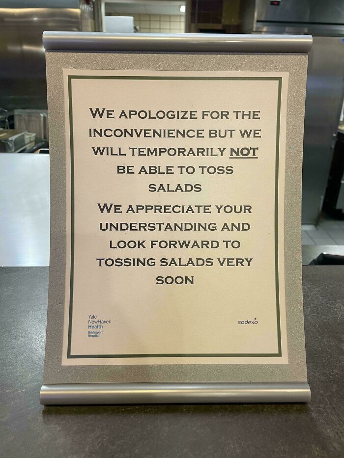 Funny sign apologizing for temporarily not being able to toss salads, displayed in a restaurant setting.
