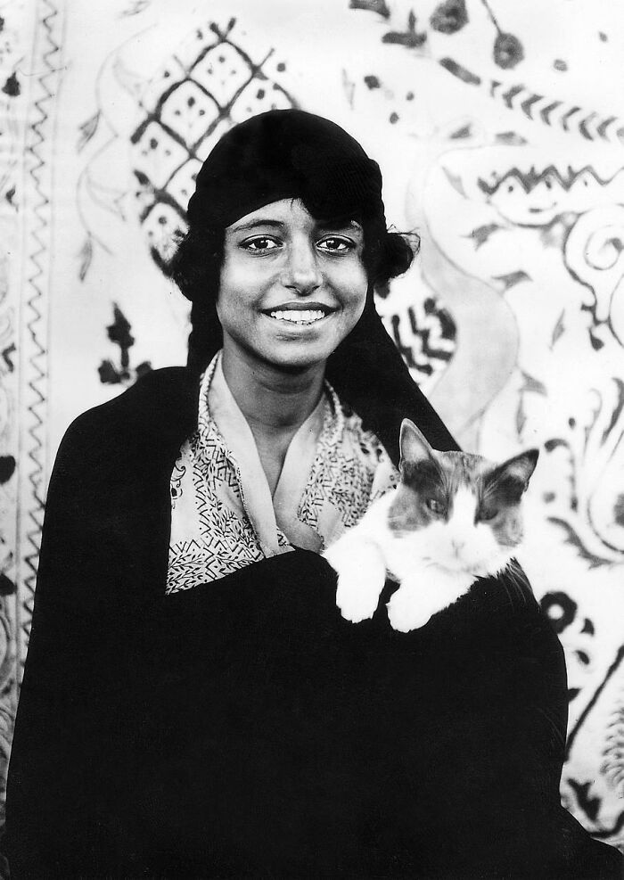 Smiling person holding a relaxed cat, showcasing vintage-cat-photos with a patterned backdrop.