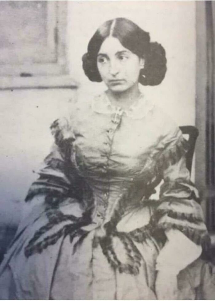 A woman in a vintage dress seated, illustrating interesting historical fashion.