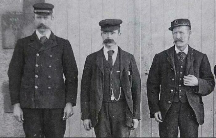 Three men in vintage uniforms and hats, standing in front of a wooden wall, showcasing interesting historical attire.