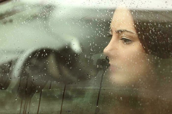 A woman looks through a rainy window, lost in thought, highlighting interesting facts.