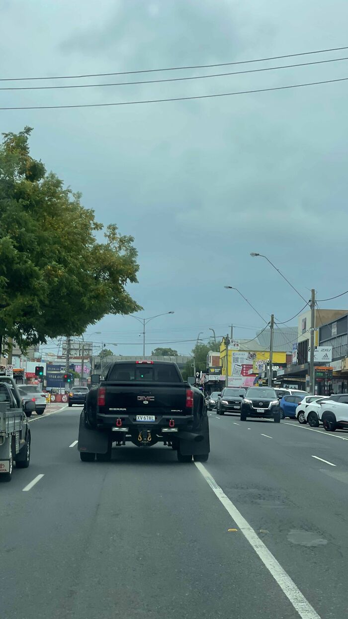 Large black pickup driving down an Australian street under cloudy skies, showcasing 'Nope' community sights.