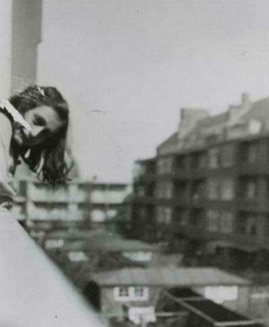 A historical photo of a person leaning out of a window in an old urban area.