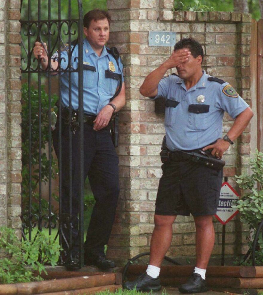 Historical photo of two police officers, one leaning on a gate, the other with a hand on his forehead outside a brick wall.
