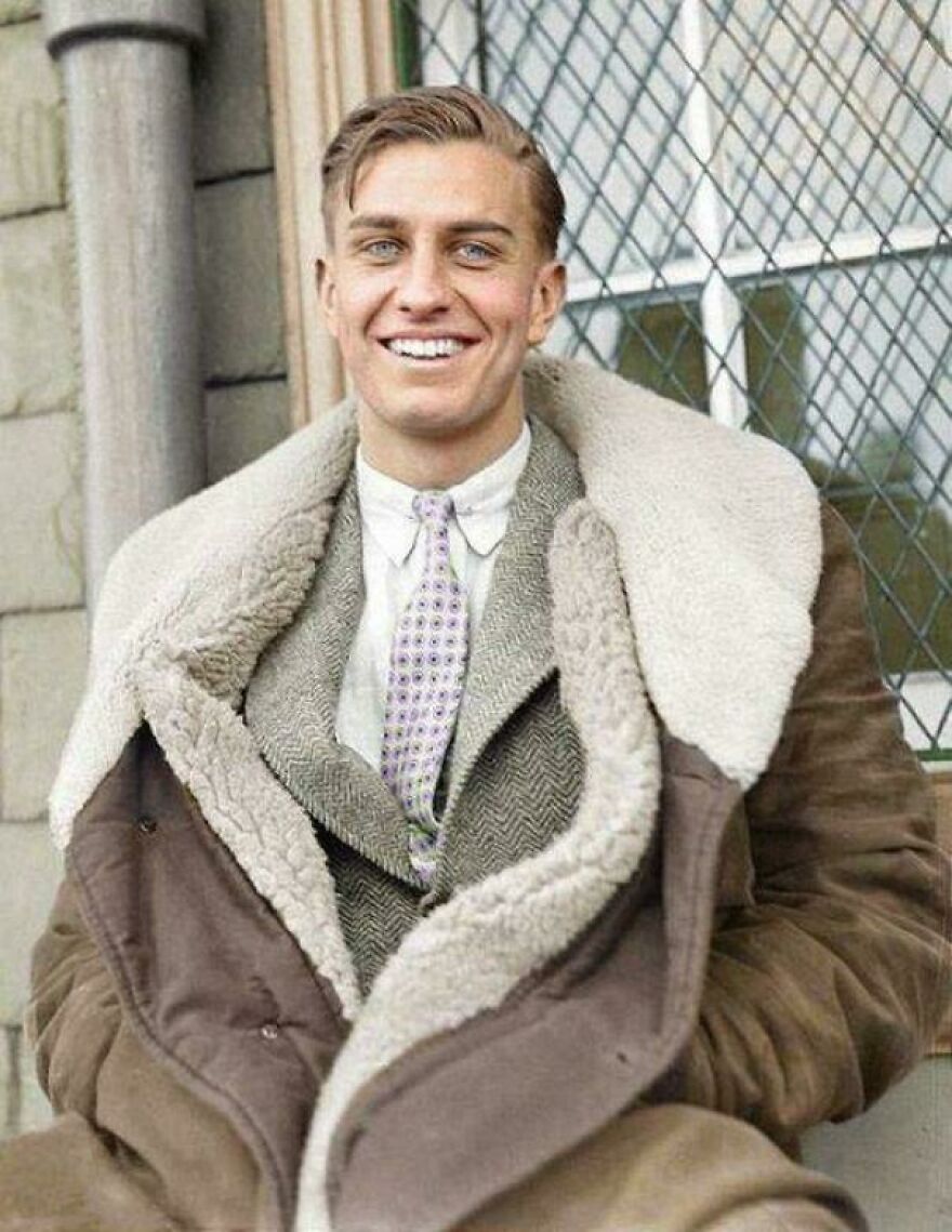 Young man in a vintage wool coat smiling in front of a window, from a collection of historical photos.
