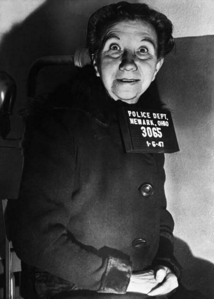 Elderly woman in historical police mugshot from Newark, Ohio, wearing a coat and looking at the camera.