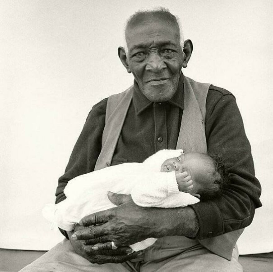 Elderly man holding a newborn, showcasing historical generational contrast in a black and white photograph.