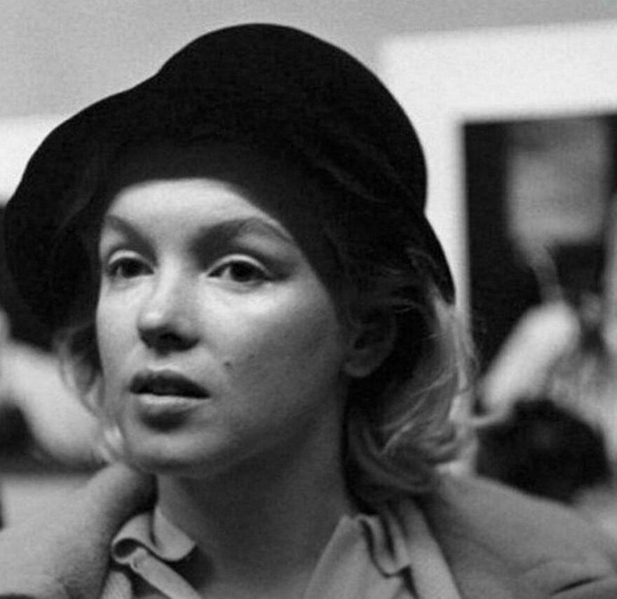 A woman in a black hat poses in a historical photo, captured in a candid moment.