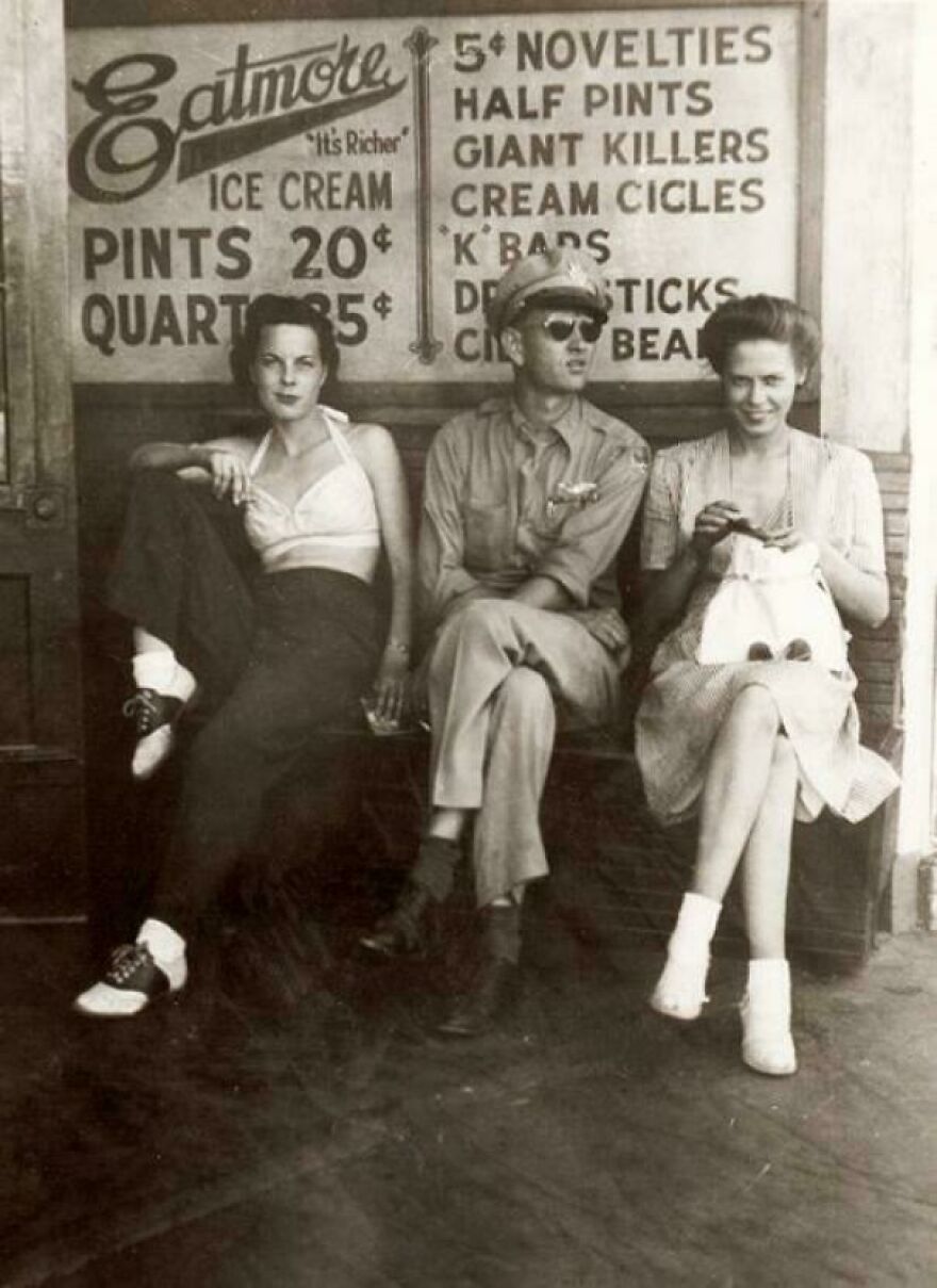 Three people sitting in front of an old ice cream shop sign, capturing a moment in historical photos.