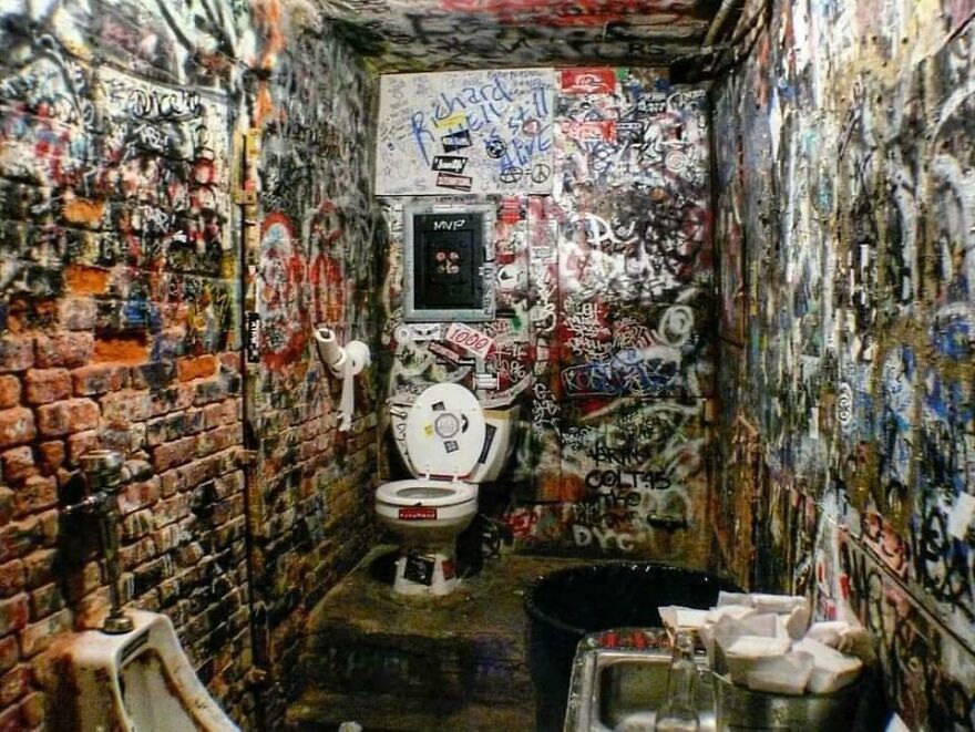 Graffiti-covered bathroom walls with a toilet and sink, showcasing historical photos and urban art.