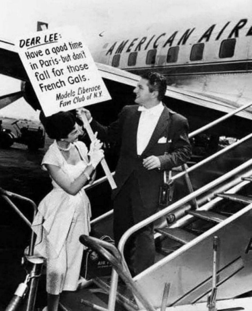 Man holding humorous sign at airplane stairs, historical moment captured.