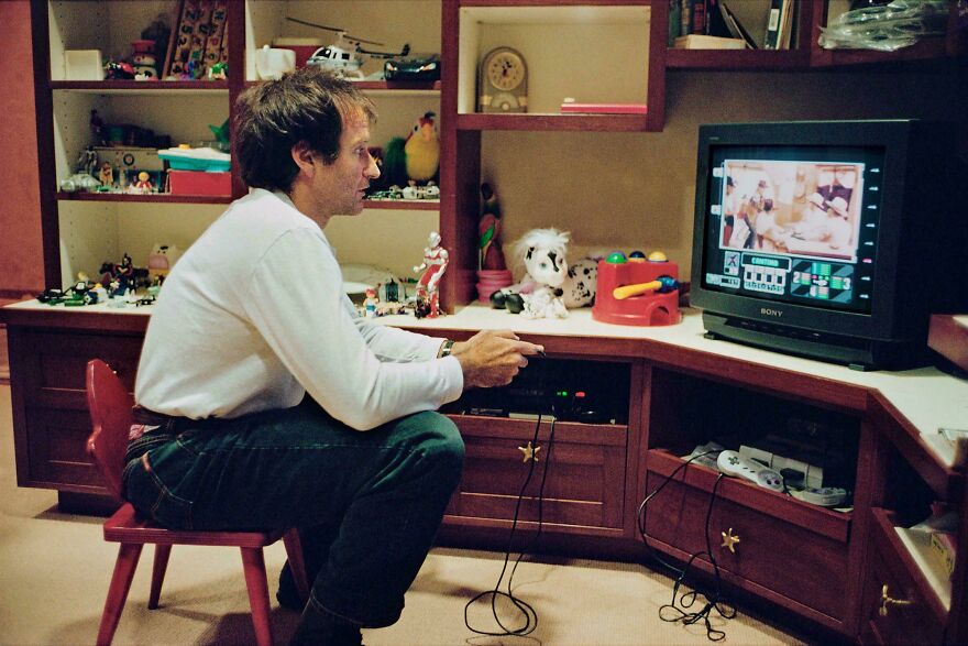 Man in a vintage setting playing a video game, featuring historical photos memorabilia on shelves.