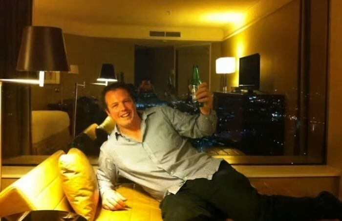 A person smiling and reclining with a bottle in hand, in a cozy room setting, sharing interesting facts.