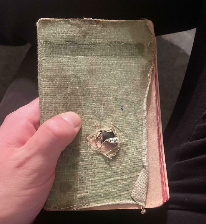 Hand holding an old, worn book with a hole in the cover, showcasing a unique find among cool-old-things.