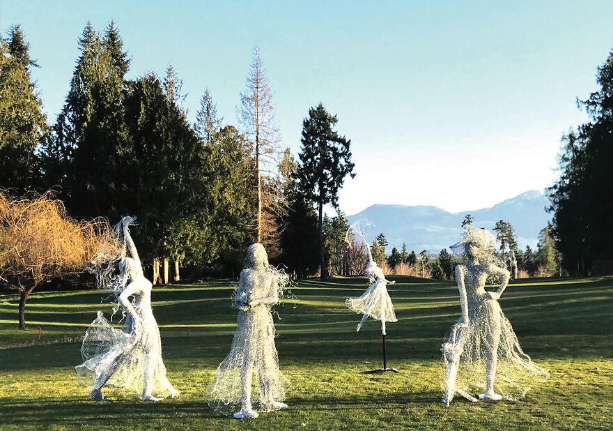 Chicken wire sculptures on a grassy field with trees and mountains in the background.