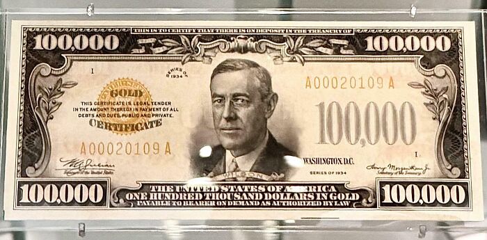Old $100,000 bill with Woodrow Wilson, displayed in a glass case.