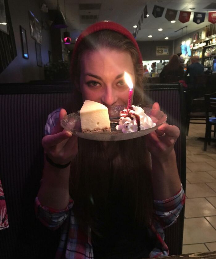 Person holding a dessert with a lit candle in a restaurant setting, conveying an eerie vibe for photographs with backstories.
