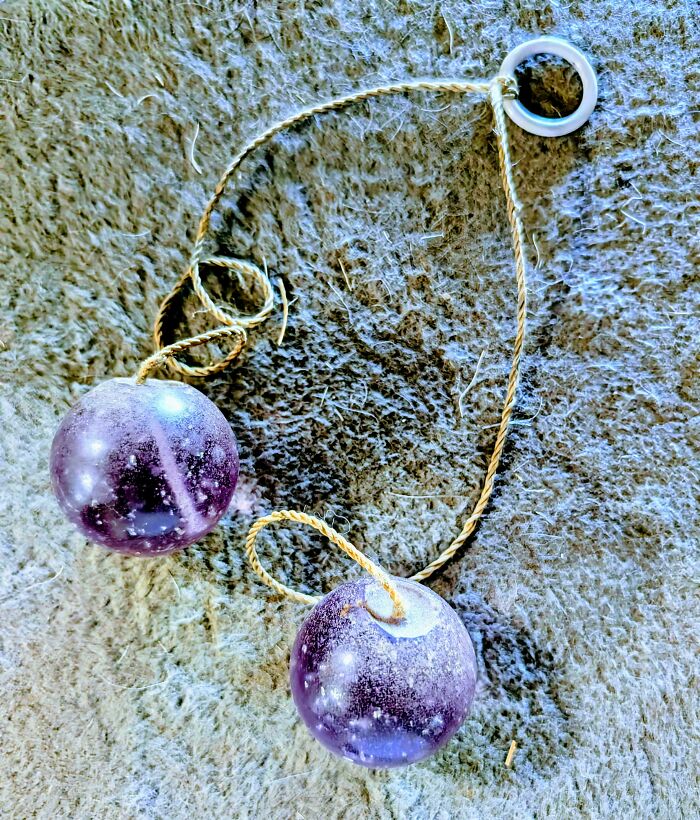 Purple toy clacker balls on a string, resting on textured fabric, evoke nostalgia and a feeling of being old.