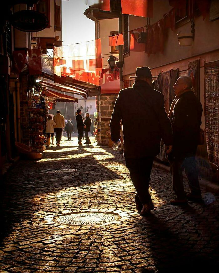 Cobblestone street with people in sunlight, resembling an accidental Renaissance painting.