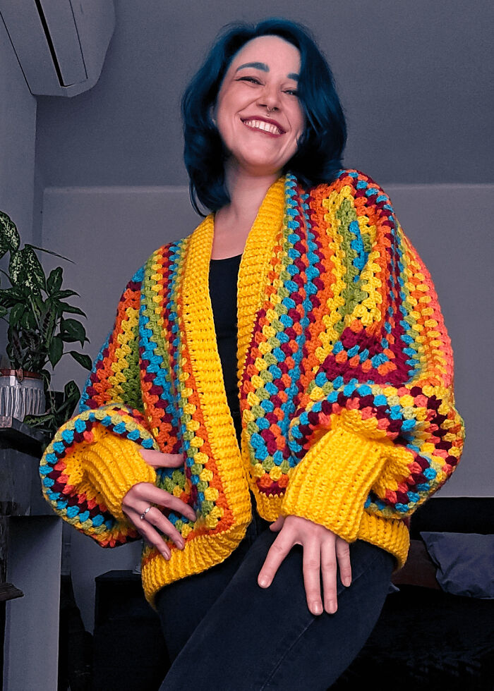 Smiling woman wearing a colorful crochet cardigan with vibrant stripes showcasing crochet masterpieces.