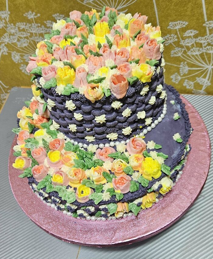 Two-tiered floral decorated cake with purple icing and pastel buttercream flowers, an incredible bake showcasing detailed craftsmanship.