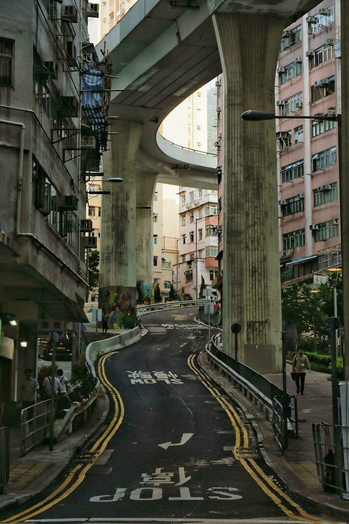 Urban hell scene with towering overpass and narrow winding street.