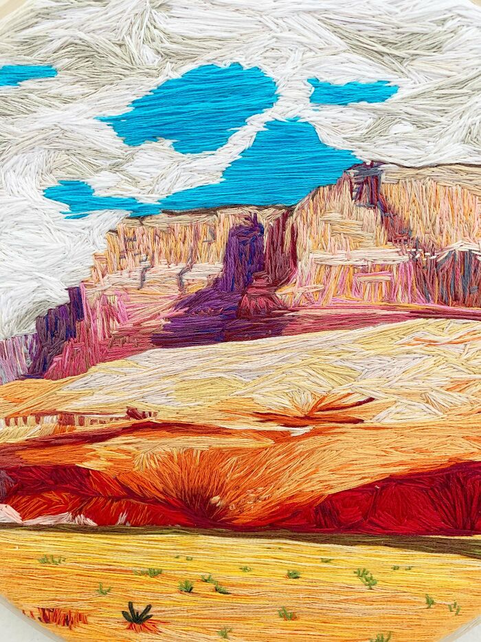 Detailed embroidery depicting a colorful desert landscape with cliffs, blue sky, and clouds showcasing incredible embroidery skills.
