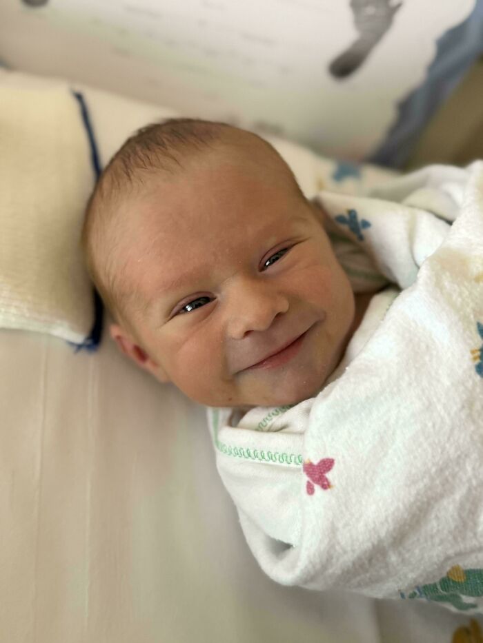 Newborn baby swaddled in a blanket, smiling gently, capturing a wholesome dad parenting moment.