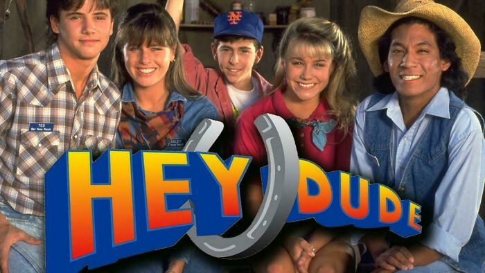 Cast of 1990s TV show Hey Dude smiling, with logo in front, celebrating 90s nostalgia.