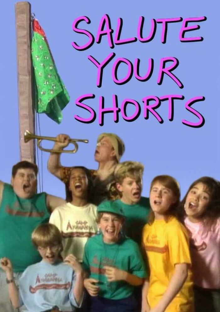 Group of kids from '90s show Salute Your Shorts, gathered with a trumpet, smiling, wearing colorful Camp Anawanna shirts.