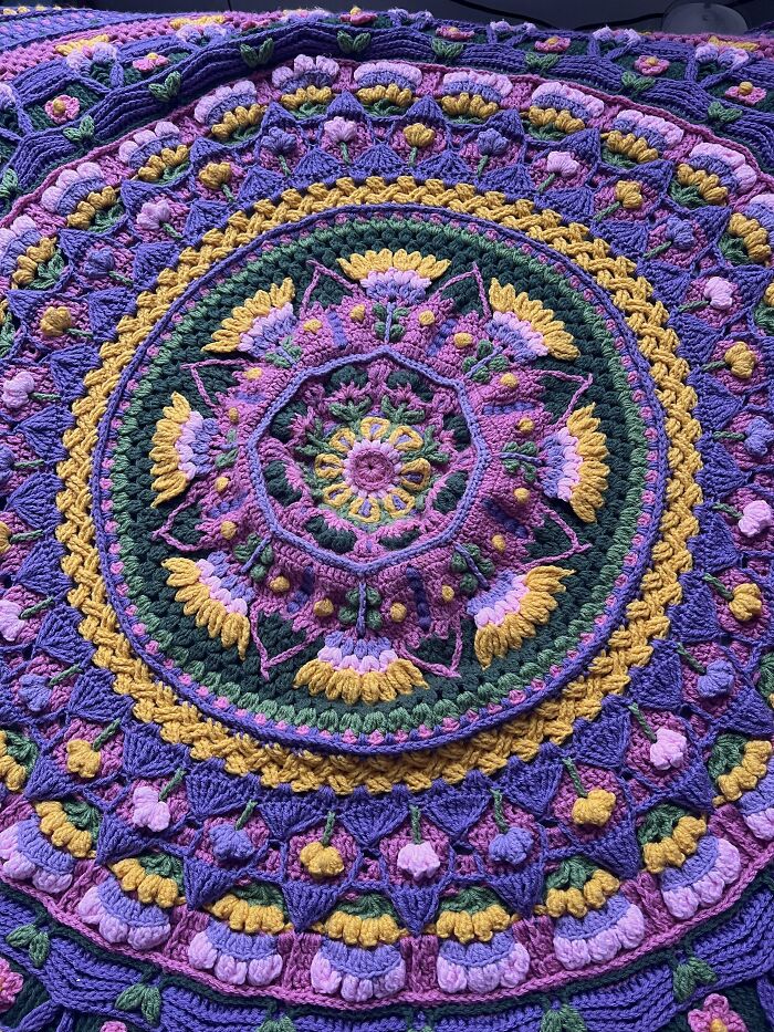 Colorful crochet masterpiece with floral patterns in purple, yellow, and green showcasing intricate crochet hook craftsmanship.