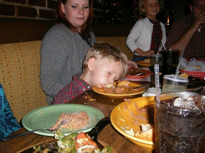 Young boy asleep with face on plate at family dinner, capturing an awkward family moment that also feels incredibly sweet.