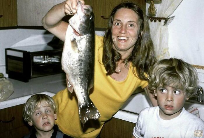 Woman holding a large fish with two young boys making awkward faces in a sweet family photo moment.