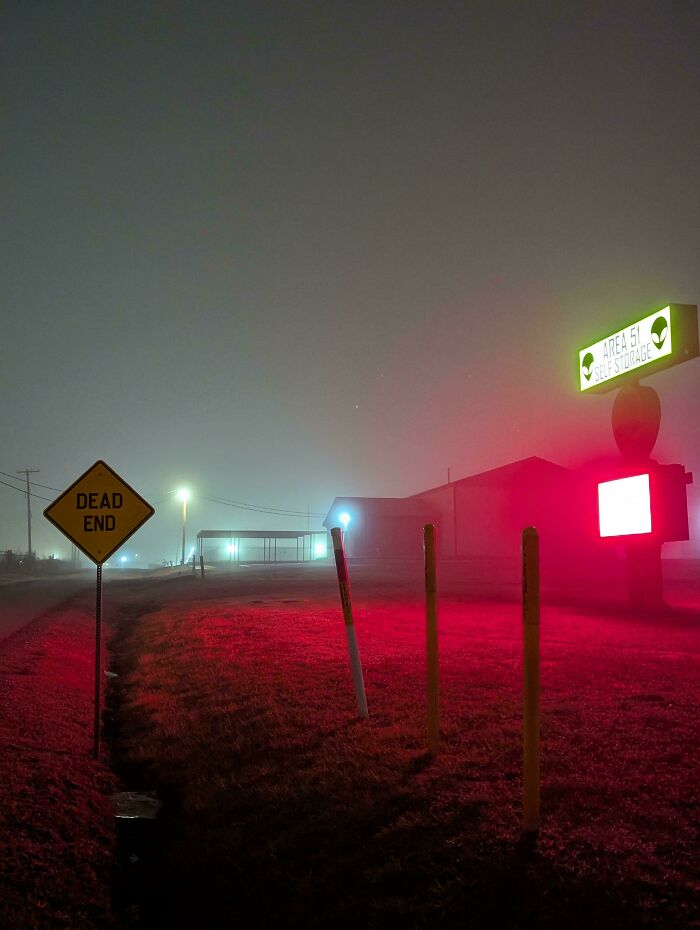 Foggy night scene with eerie red lighting near a building, featuring signs for Area 51 and a dead end road.