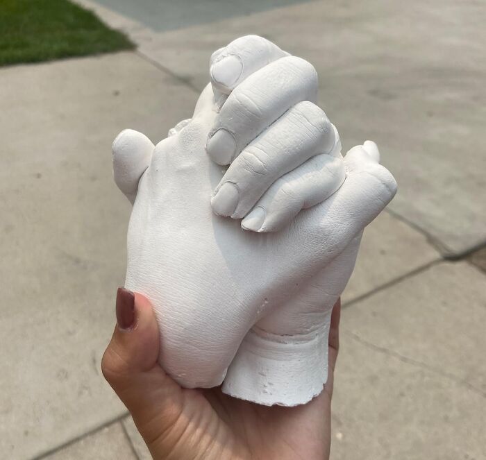 Plaster sculpture of two hands clasped together, symbolizing V-Day for long term couples, held outdoors.