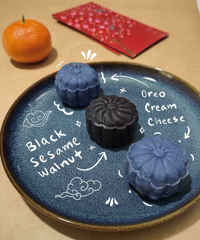 Blue and black mooncakes labeled black sesame walnut and oreo cream cheese on a dark blue plate, showcasing incredible bakes.