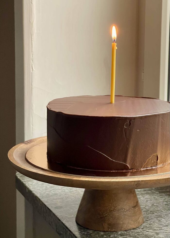 Chocolate cake with smooth frosting and a single lit candle on a wooden stand, showcasing incredible bakes.